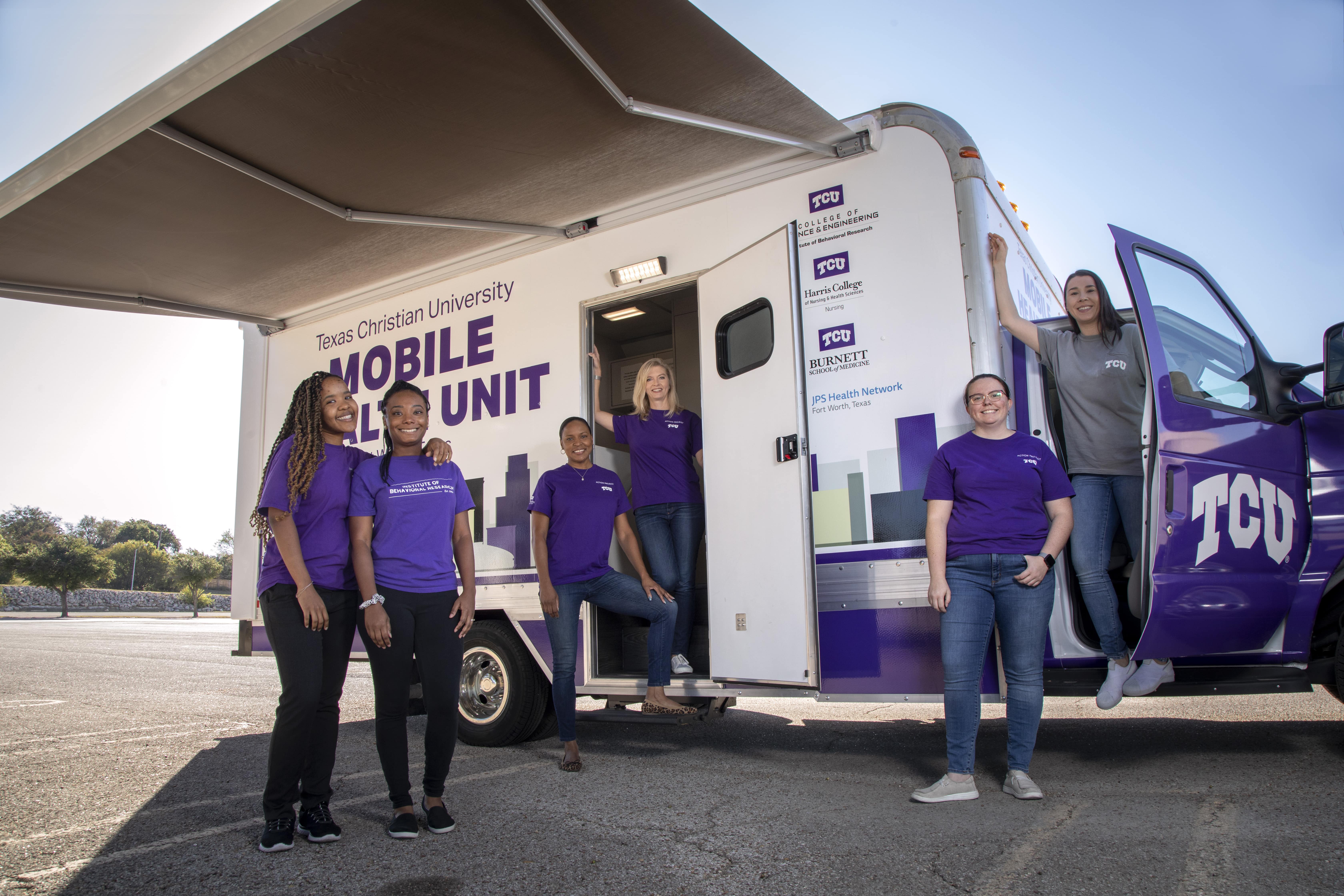 Students and faculty all wearing purple and standing beside the TCU Mobile Clinic van